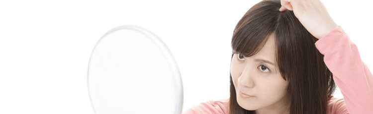 Woman examining her hairline at the top of her head in the mirror