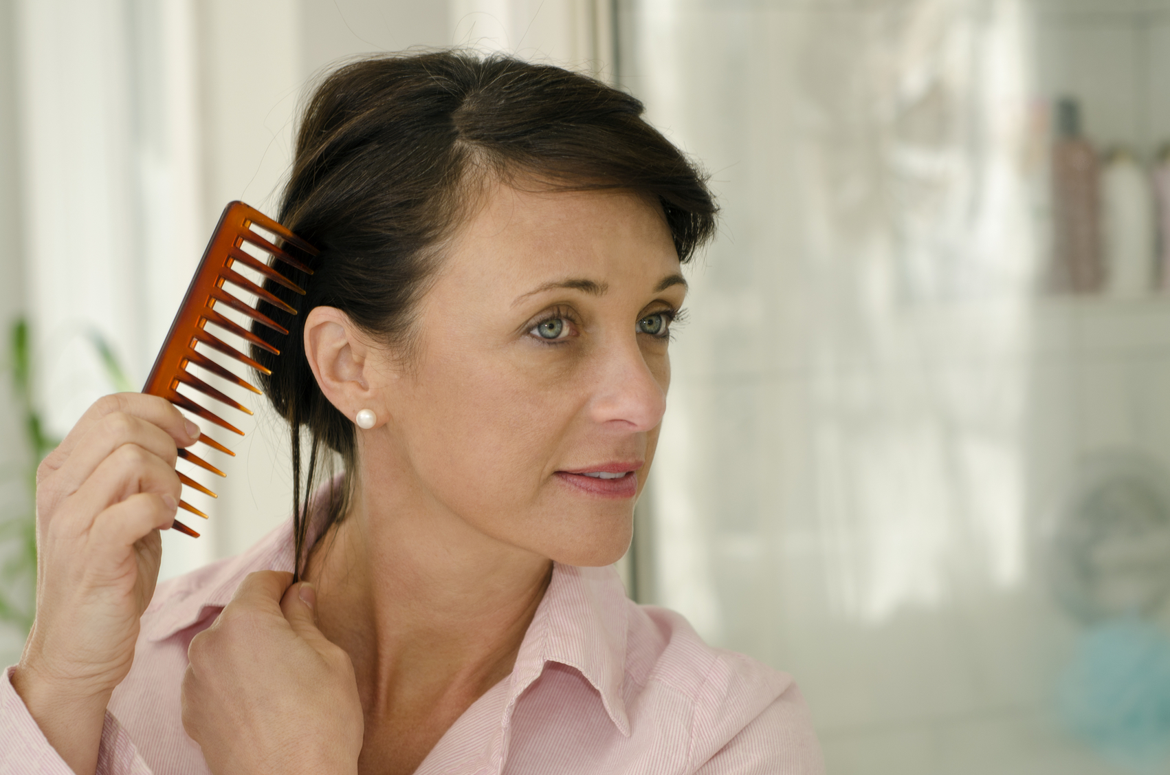 A woman in a pink shirt combs her hair