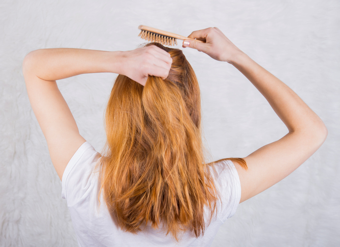 Red-haired young woman combing hair with wooden comb.